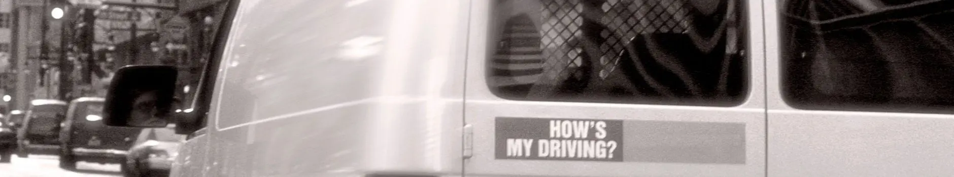 Black and white photo of back of a van with "How's my Driving?" sticker