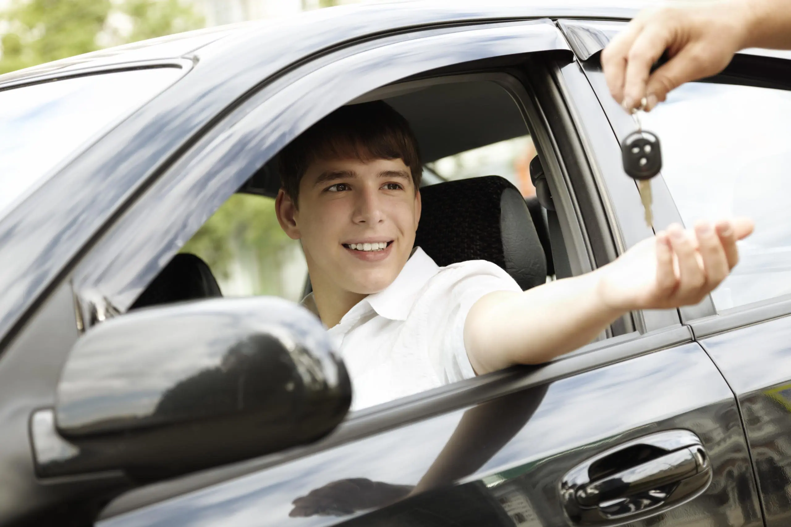 Teen smiling and receiving car keys from an adult in a car.