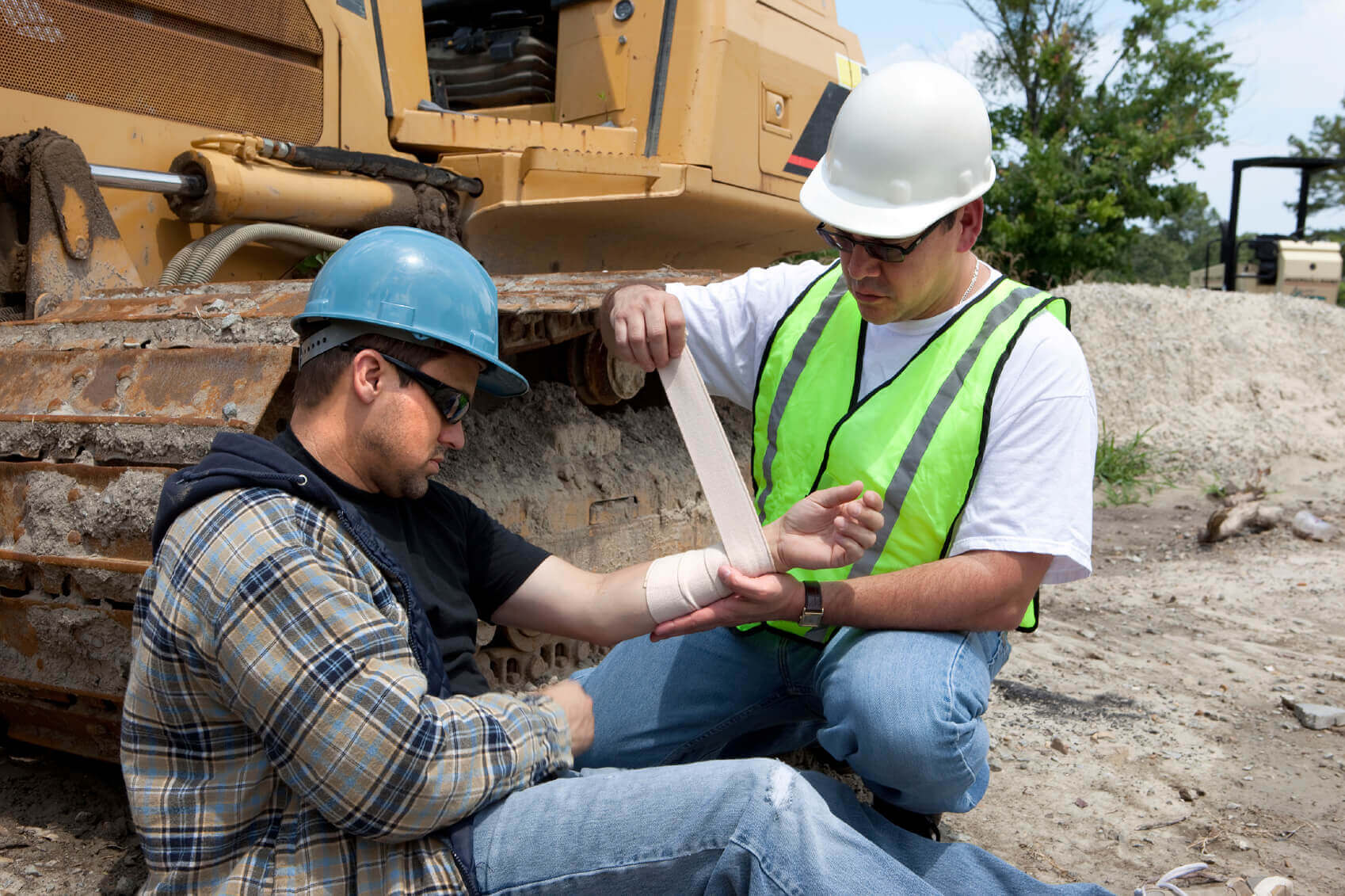 Construction worker providing first aid bandaging to injured worker.