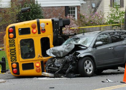 Car crash with bus flipped on its side and gray sedan with hood damage