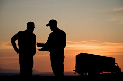 Silhouette of two men signing a document in front of a truck