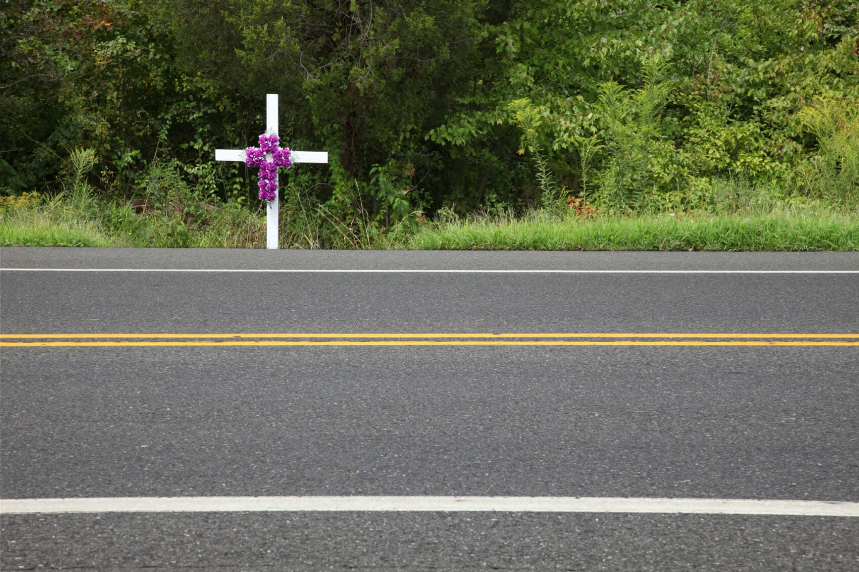 A white cross with roses on it alongside a road