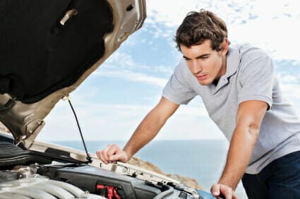 Young man looks under the hood of his car for engine trouble.