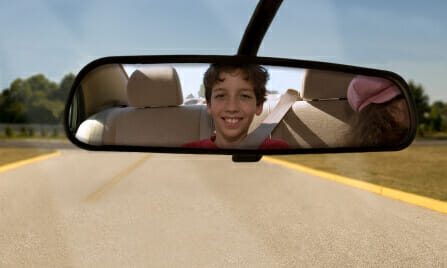 Child looking and smiling into rearview mirror
