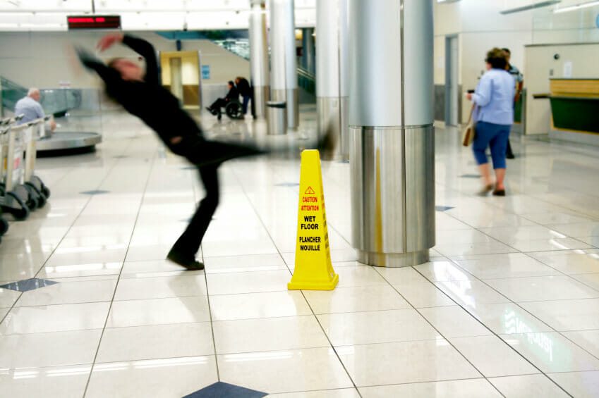 Person in shopping center slipping and falling next to a caution wet floor sign