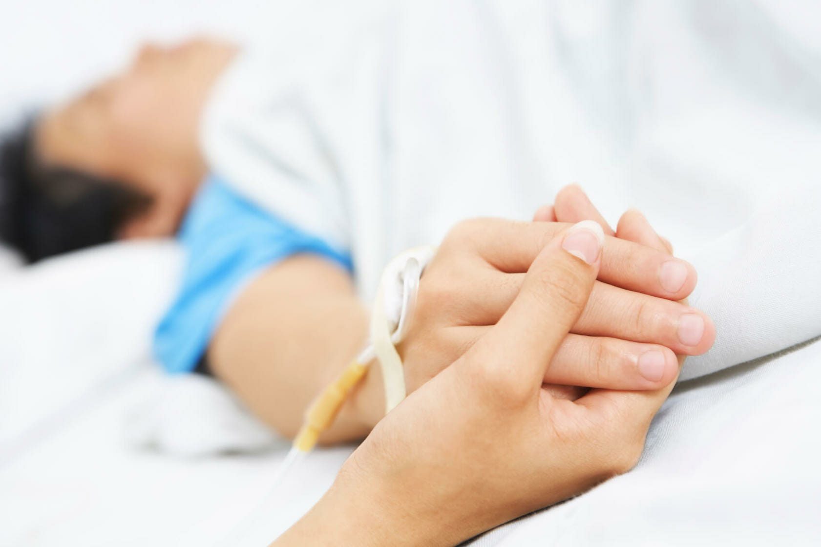 Person holding the hand of an injured patient lying in a hospital bed