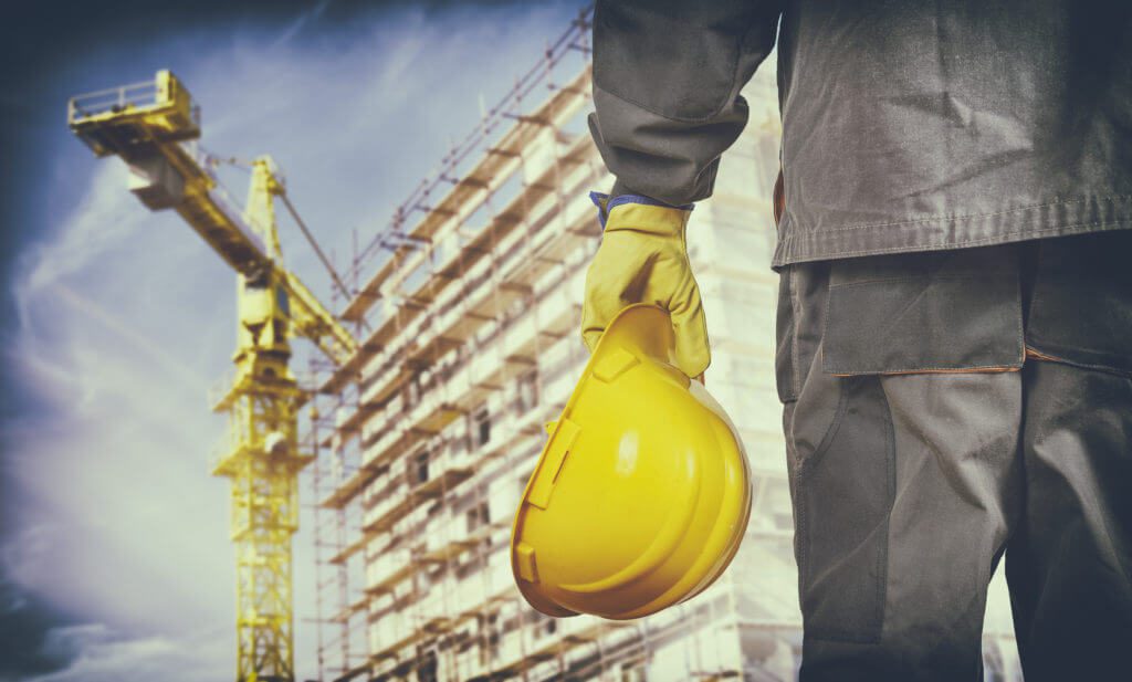 Construction worker with protective uniform in front of construction scaffolding and construction crane