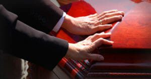 Two people with their hands placed on a casket at a funeral.