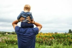 Father holding up child on shoulders in flower field