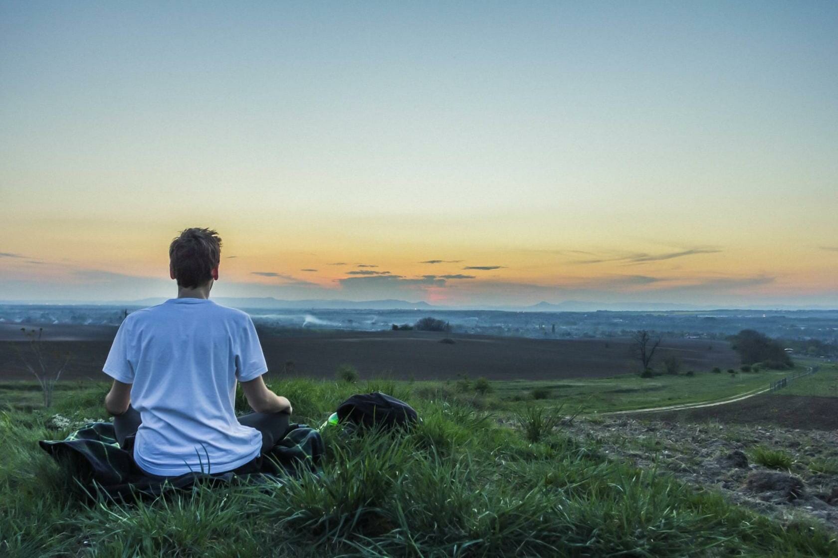 Man meditation on field looking at sunset