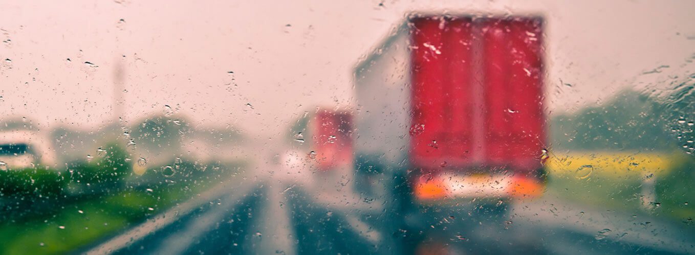 Two trucks driving down road on a rainy day